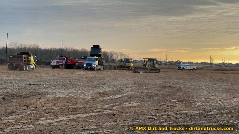 Dump truck dumping fill dirt at golden hour on Houston land development site, fleet and bulldozer in background