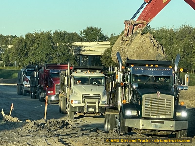 Dump truck fleet lined up and getting loaded by excavator at golden hour on Houston jobsite